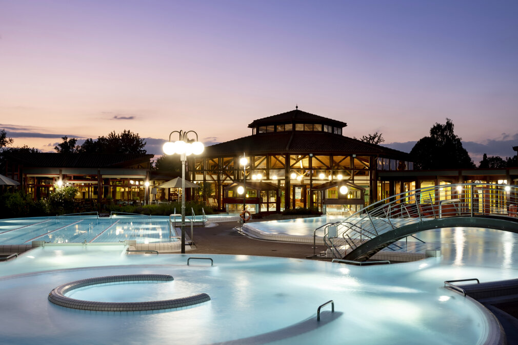 Thermalbad Sonnenhof-Therme bei Dämmerung mit beleuchteten Außenpools, einem modernen Gebäude im Hintergrund und entspannter Atmosphäre.