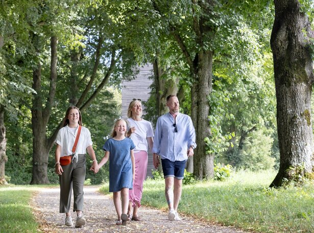 Familie mit zwei Erwachsenen und zwei Kindern geht auf einem von Bäumen gesäumten Weg auf der Schillerhöhe Bad Saulgau spazieren
