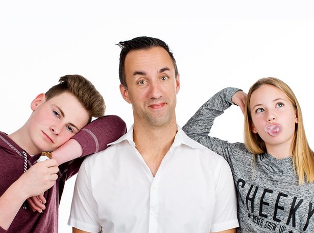 Mittelalter Mann in weißem Hemd, der teils genervt teils belustigt in die Kamera sieht, an seiner rechten Schulter lehnt ein Teenager, der genervt in die Kamera sieht, an der linken Schulte eine Teenagerin, die zur Seite sieht und eine Kaugummiblase macht.