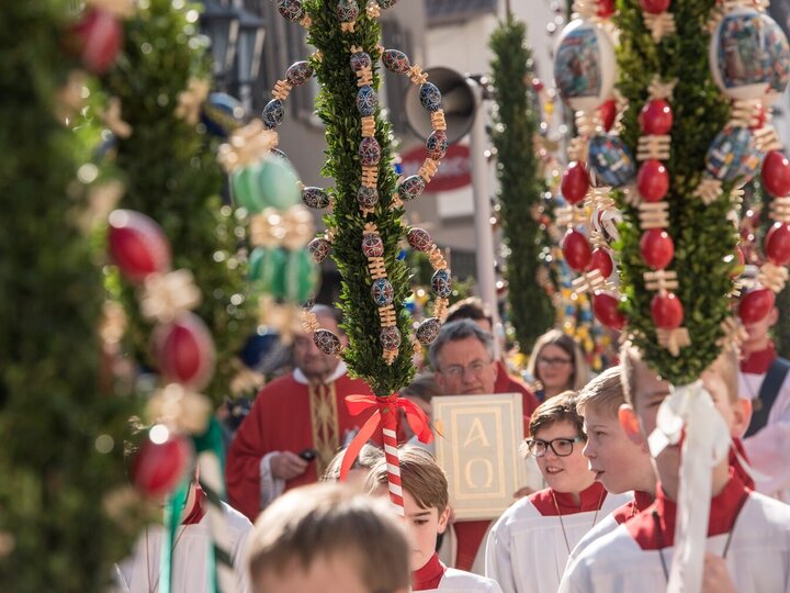 Ministranten tragen an langen Holzstäben befestigte Palmzweige durch die Altstadt